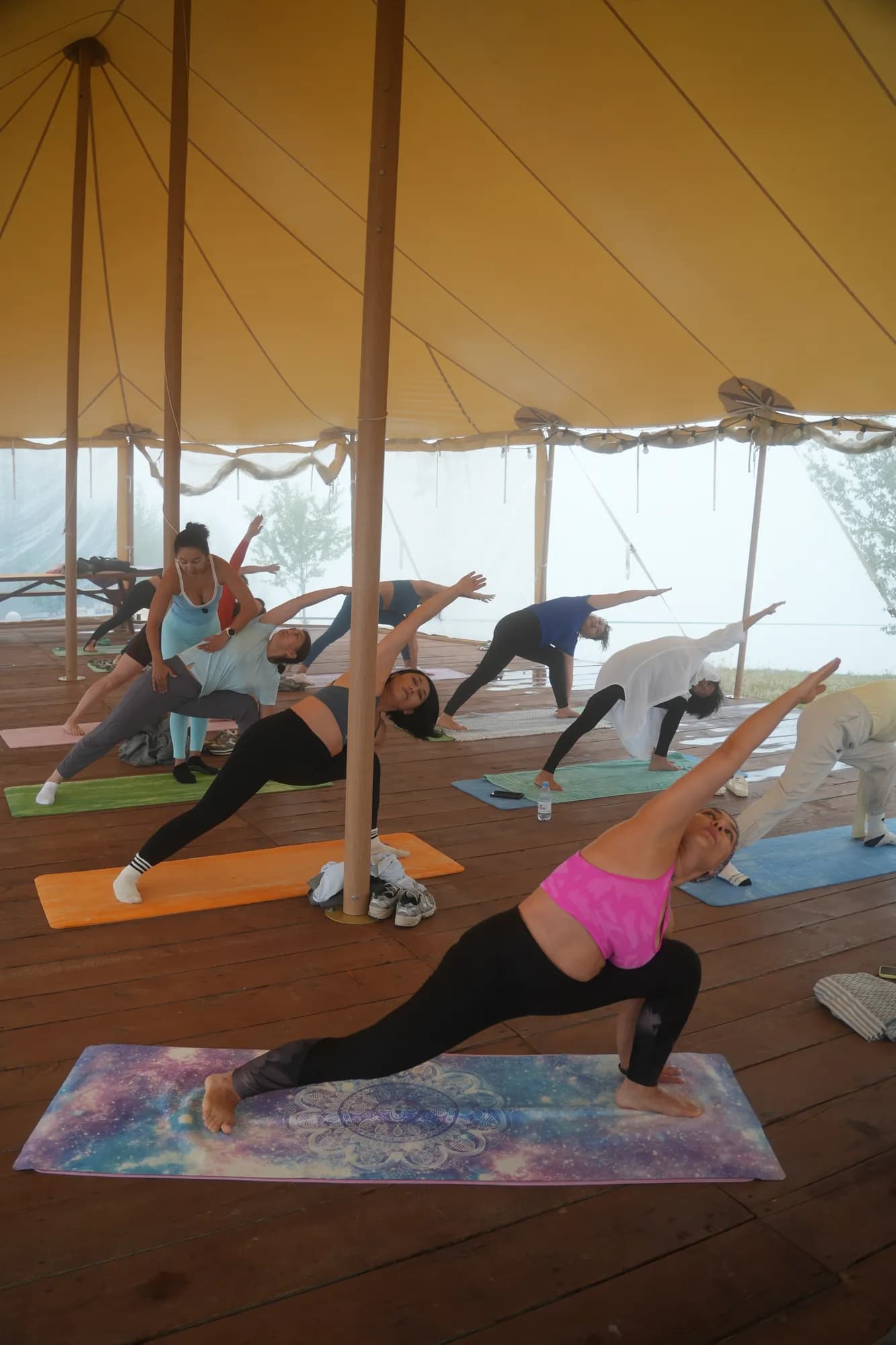 A group practising yoga on the wooden platform under the sailcloth tent