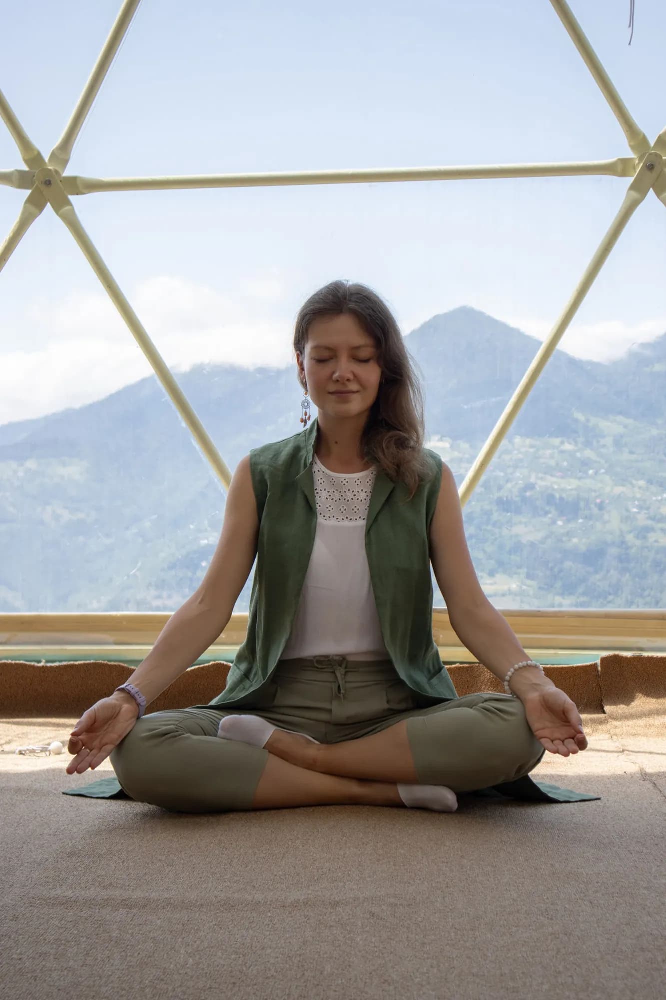 A woman meditating in the yoga dome, the mountains behind the glass