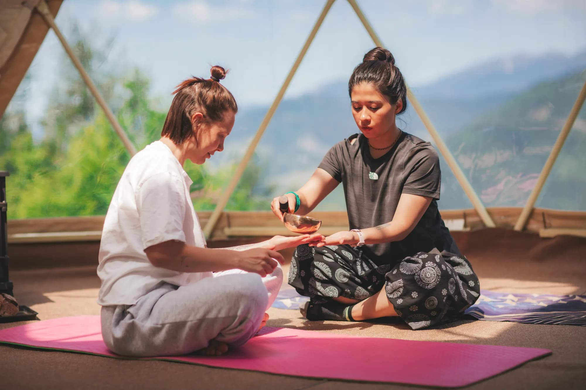 Two people on yoga mats in the dome, one holding a singing bowl