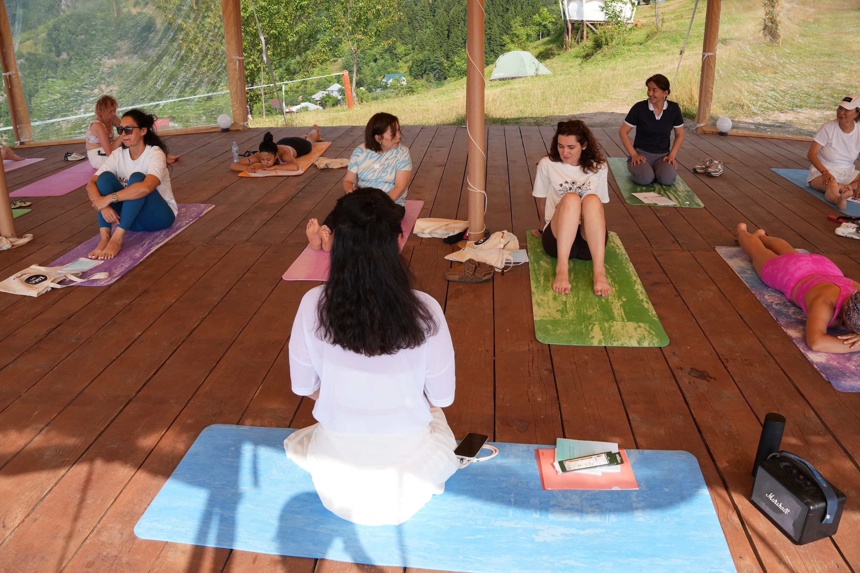 Group of people practicing yoga on mats on a wooden deck outdoors, Glamping Tago, Georgia.