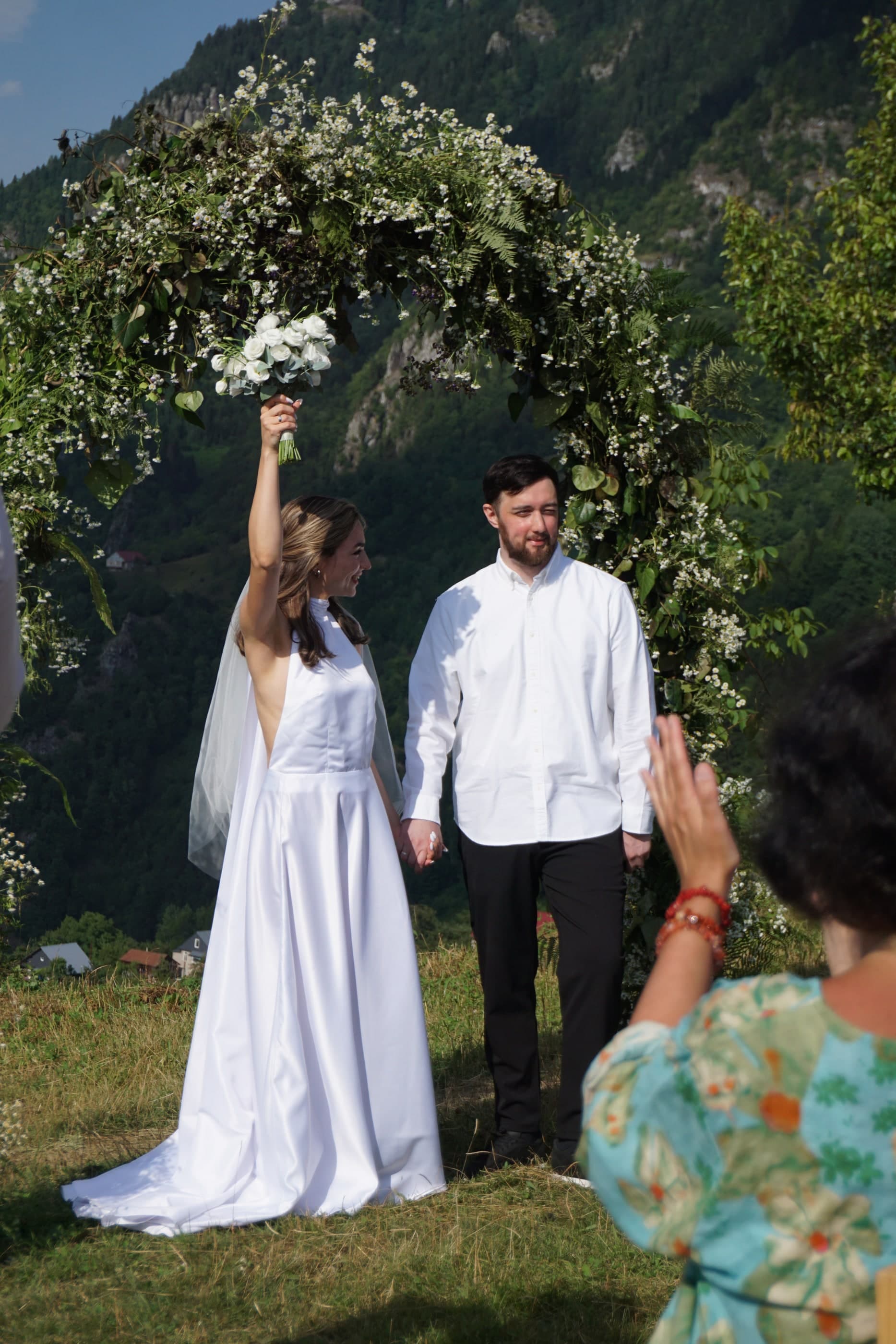Outdoor mountain wedding with couple under floral arch, bride holding bouquet, Glamping Tago, Georgia.